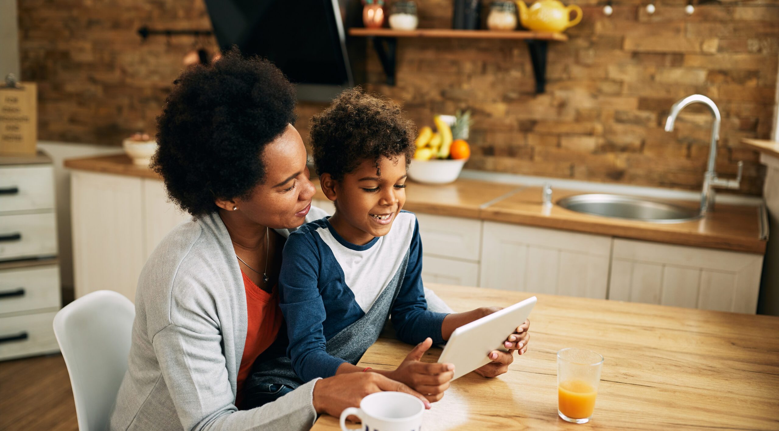 Happy African American mother and son using digital tablet while relaxing at home.